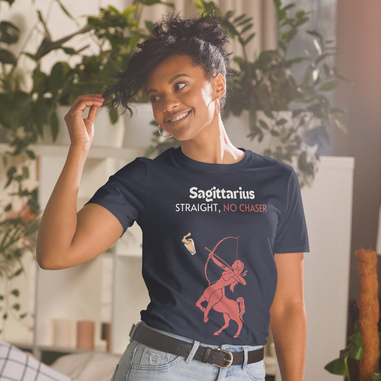 model wearing navy t-shirt lying flat on a light background, featuring a bold "Sagittarius - Straight, No Chaser" design. The graphic showcases a red centaur archer aiming at a drink, embodying the fearless and straightforward nature of Sagittarius.