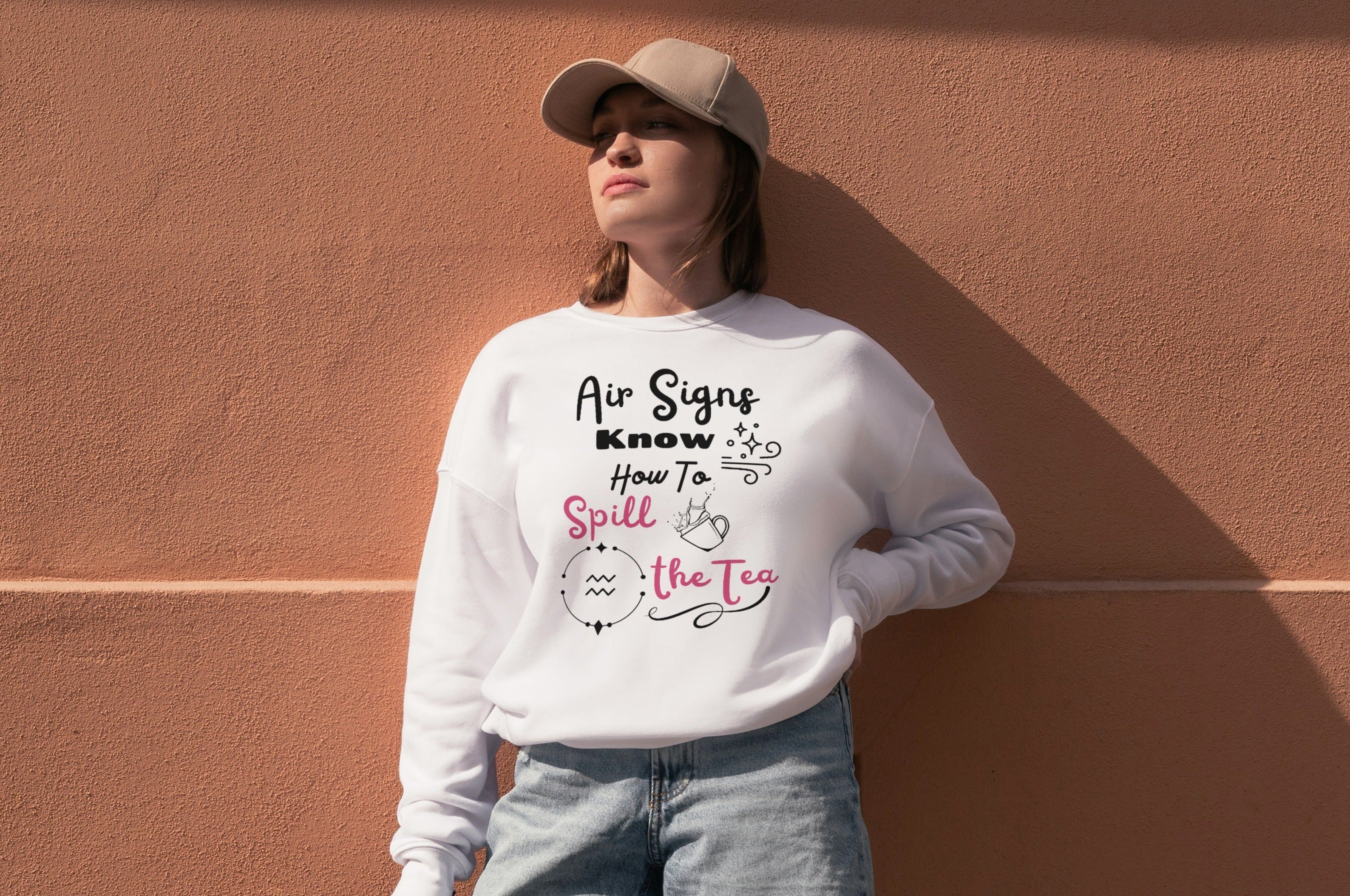 Woman wearing white sweatshirt with black and pink text that says air signs know how to spill the tea. Aquarius astrology symbol with splashing teacup