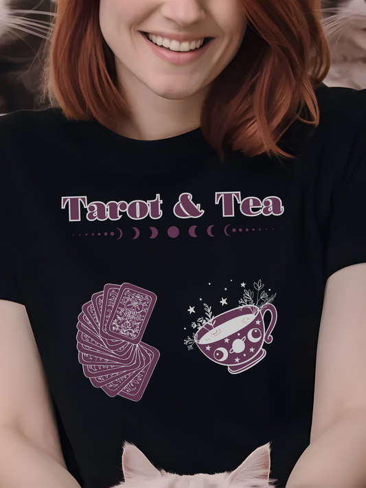 woman wearing a black t-shirt with the words "Tarot & Tea" at the top, followed by a row of moon phases. Below the text are illustrations of a deck of tarot cards on the left and a whimsical tea cup with stars and sparkles on the right.