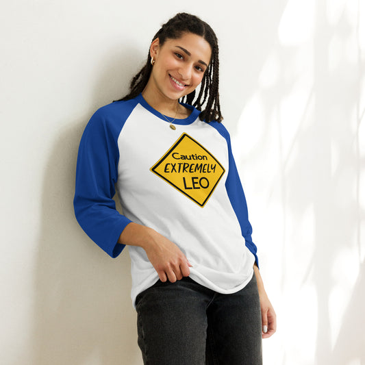 A smiling person wearing a raglan shirt with bold blue sleeves and a yellow sign that reads "Caution: Extremely Leo."