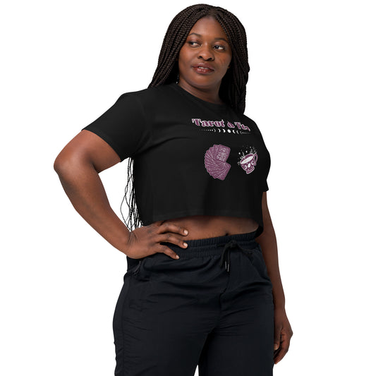 "A young woman wearing a black crop top with a whimsical 'Tarot & Tea' design, featuring illustrated tarot cards and a mystical teacup, paired with light denim shorts."